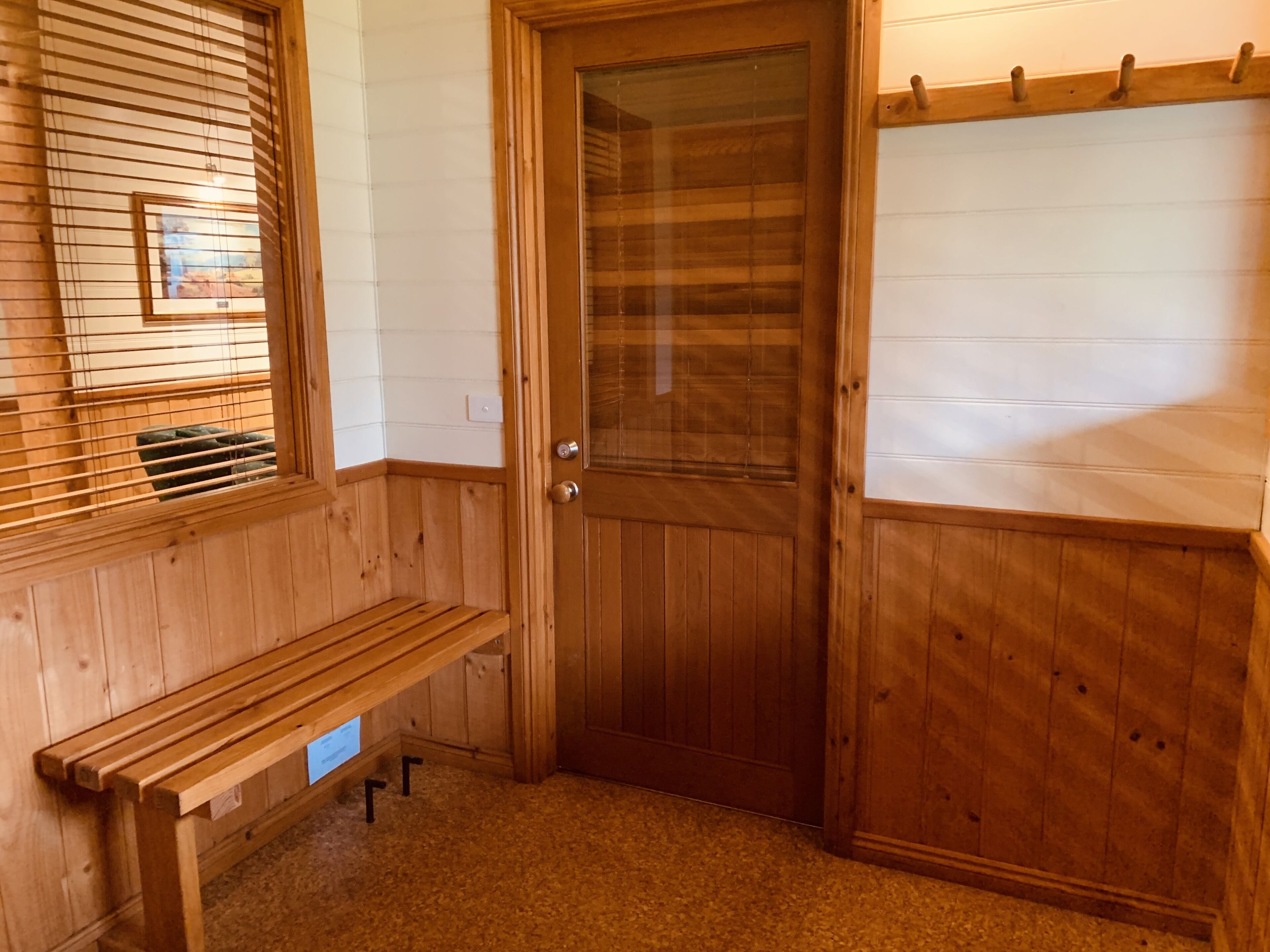 Una habitación de madera con un banco, una puerta y una ventana con persianas.