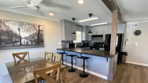 A modern kitchen with a central island, bar stools, and a dining table with chairs.