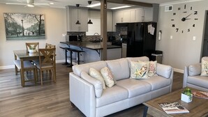 A modern living room with a sofa, coffee table, and dining area with chairs and a kitchen in the background.
