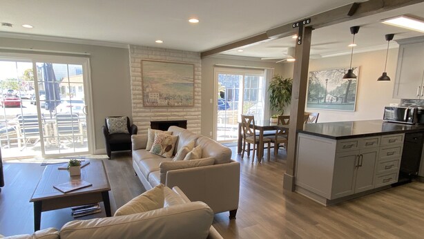 A spacious living room with a sofa, a coffee table, and a fireplace. There is a dining area with a table and chairs, and a kitchen with cabinets and a microwave.