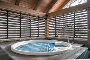Un jacuzzi en una cabaña de madera con techo inclinado y barandillas de metal.
