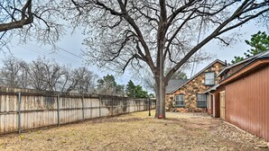 A residential backyard with a wooden fence, a large tree, and a stone building.