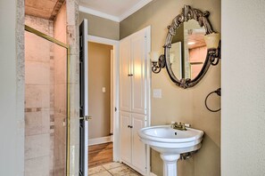 Un bagno con un lavabo bianco su piedistallo, uno specchio con cornice decorata e una porta che dà su un corridoio.
