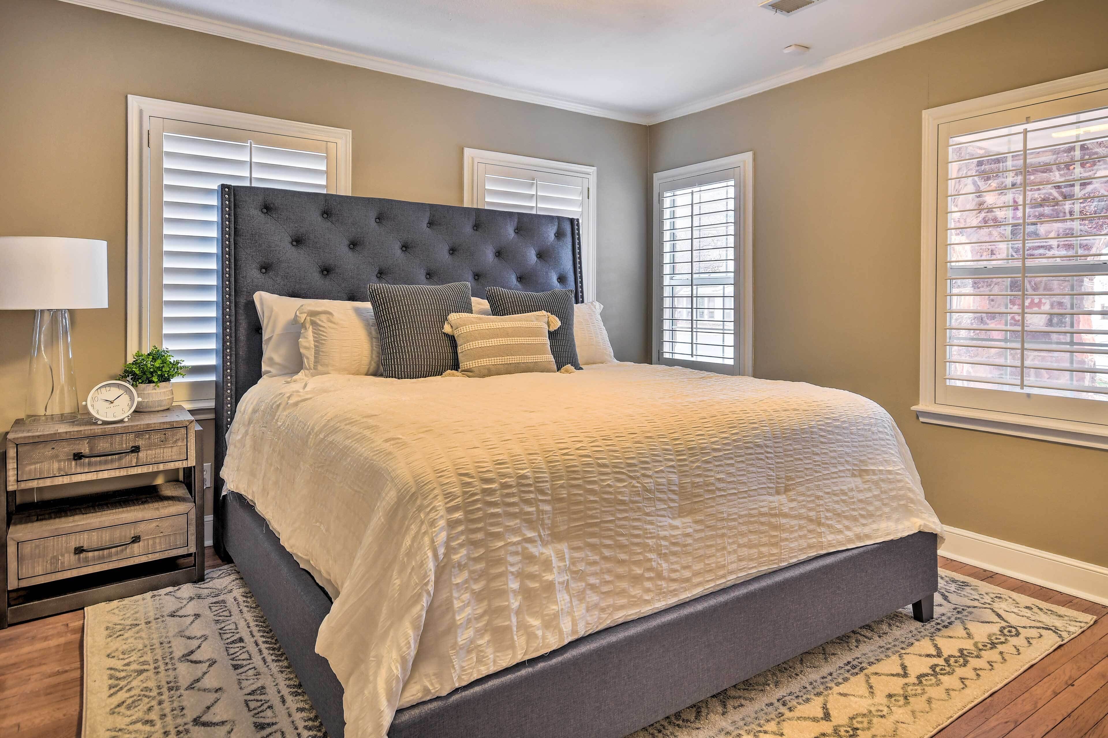 A bedroom with a large bed, a nightstand, a lamp, and a window with blinds.
