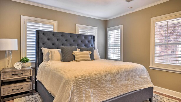 A bedroom with a large bed, a nightstand, a lamp, and a window with blinds.
