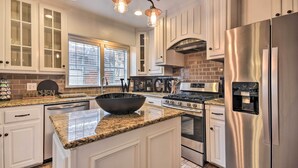A modern kitchen with white cabinetry, a large island with a black bowl, stainless steel appliances, and pendant lighting.