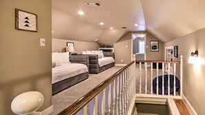 Ein Schlafzimmer mit einem großen Bett, einem kleineren Bett und einem Schreibtisch mit Stuhl. Eine Treppe mit Geländer führt zu einer oberen Ebene.