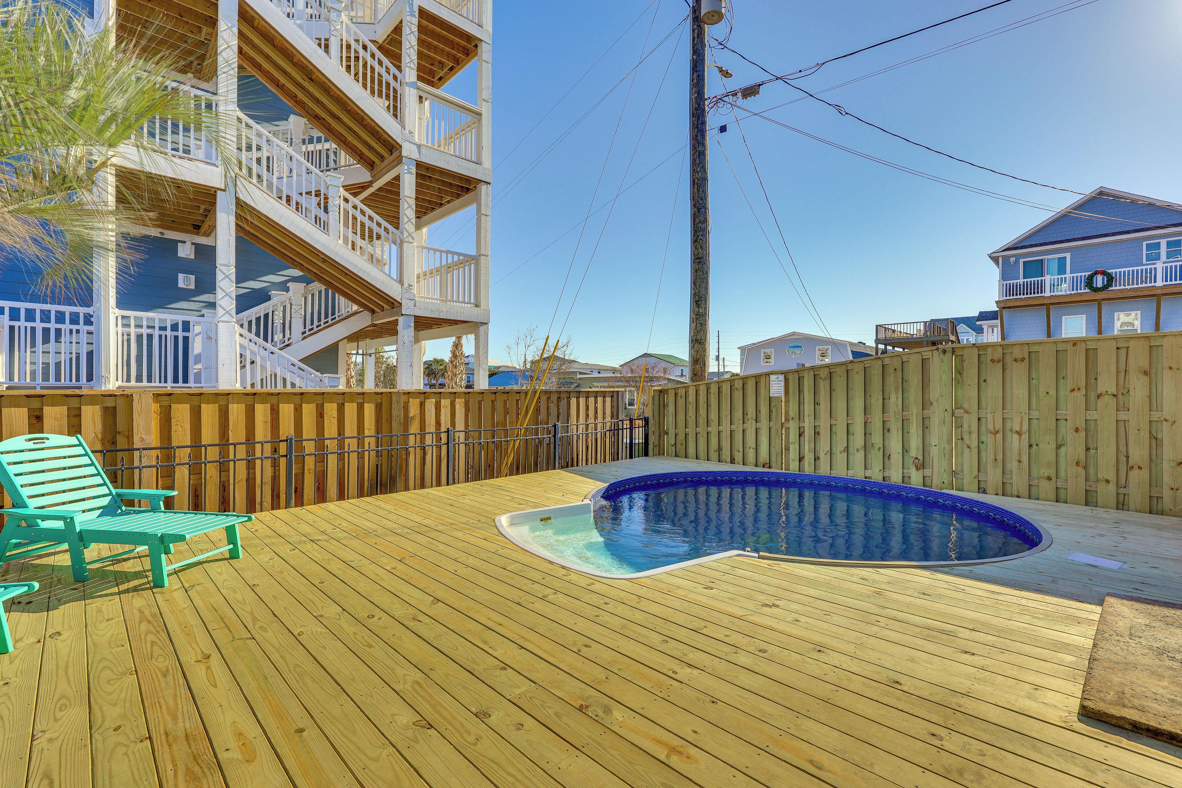 Une terrasse en bois avec une piscine, une clôture en bois et un immeuble à plusieurs étages doté de balcons.