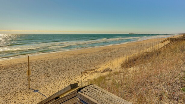 Ein Strand mit einer Holzpromenade und einem Pier in der Ferne.