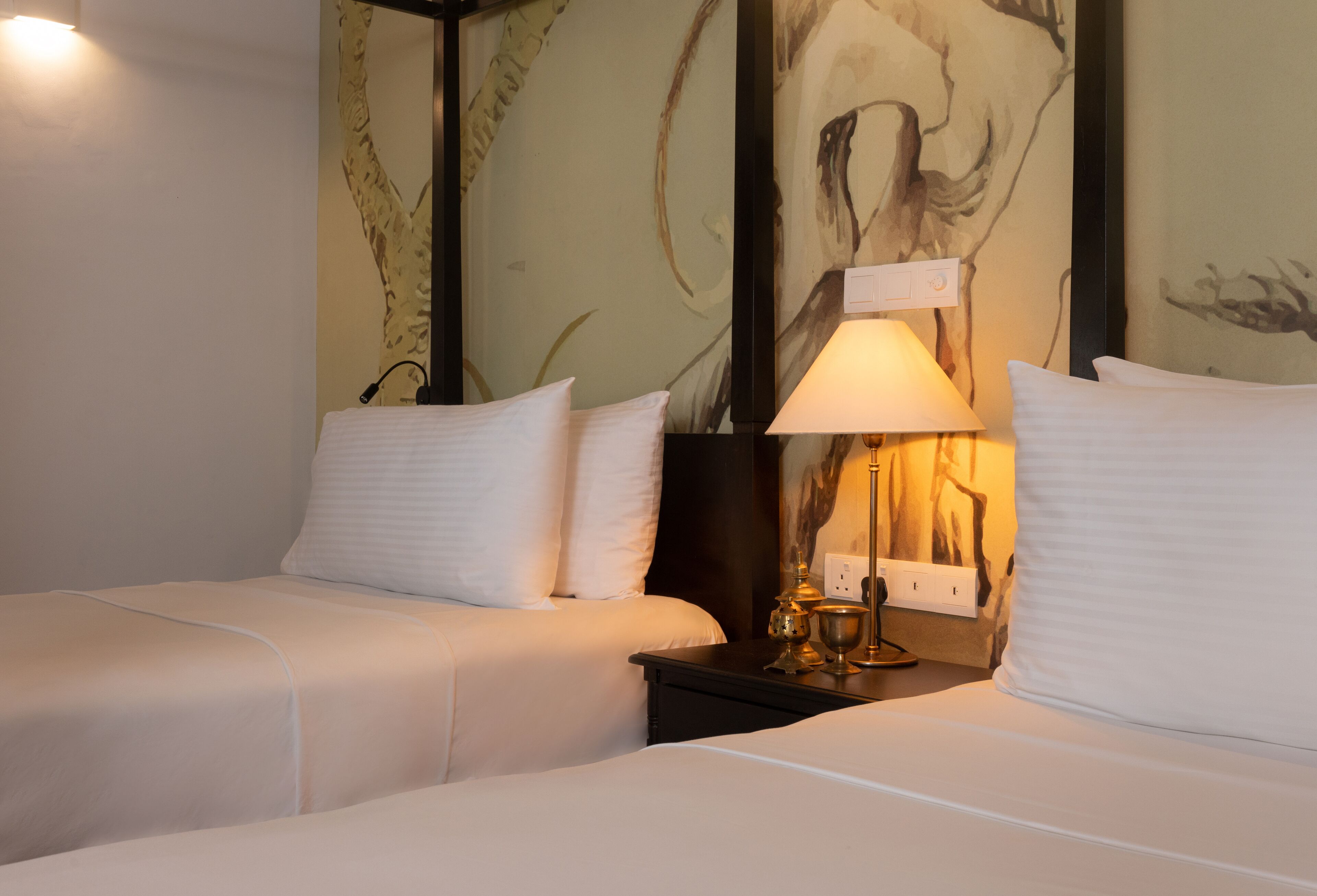 Habitación de hotel con dos camas, una mesita de noche con lámpara y una pared decorada con arte abstracto.