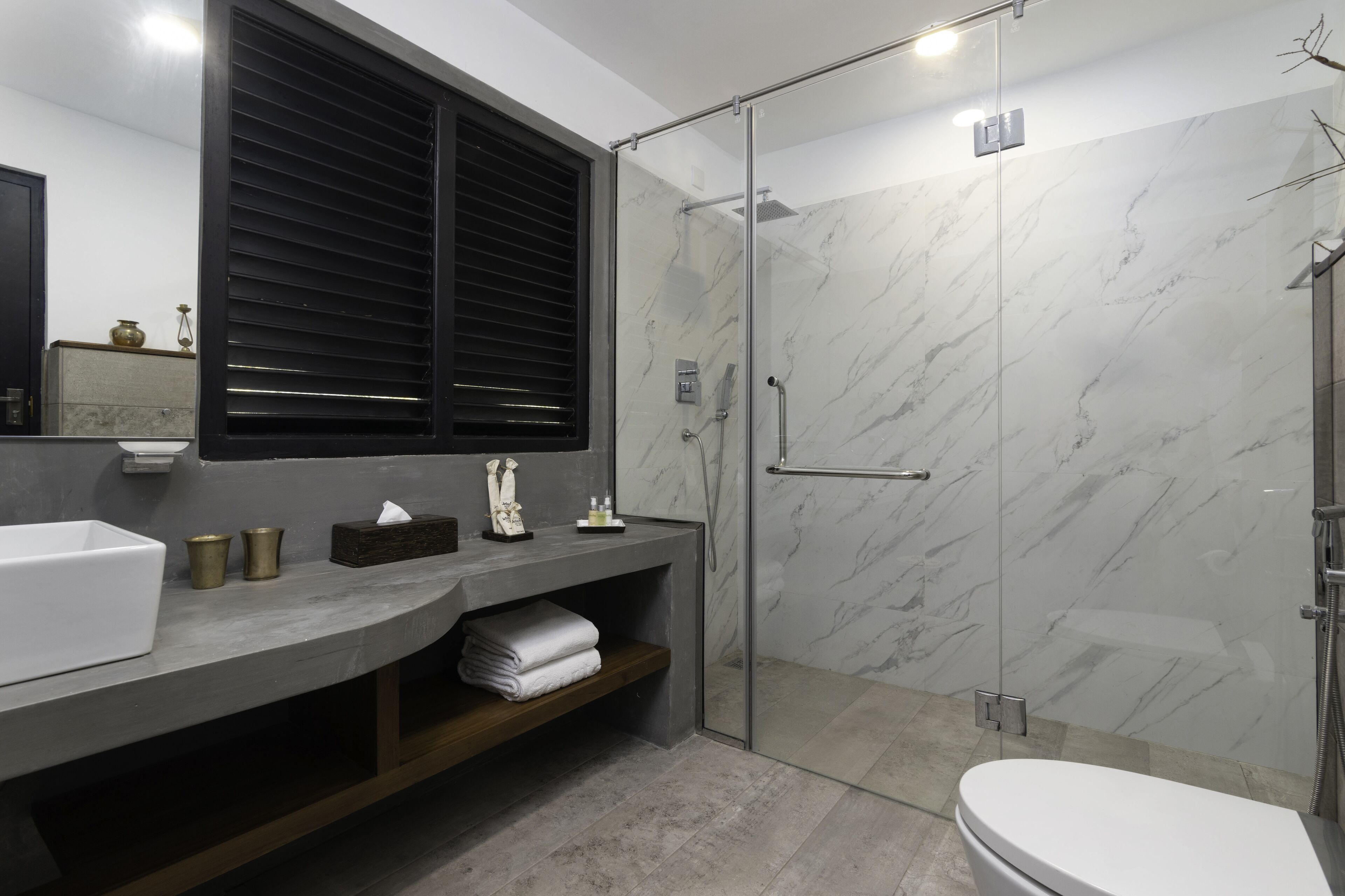 A modern bathroom with a marble shower, a glass-enclosed walk-in shower, a white toilet, and a vanity with a mirror and storage.