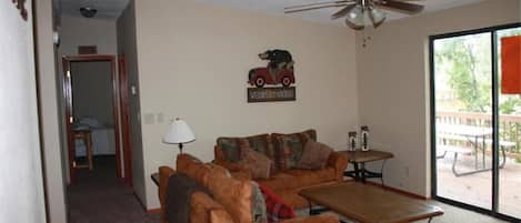 A family room with a sofa, coffee table, and a ceiling fan. A sign on the wall reads "Welcome to Mountains."