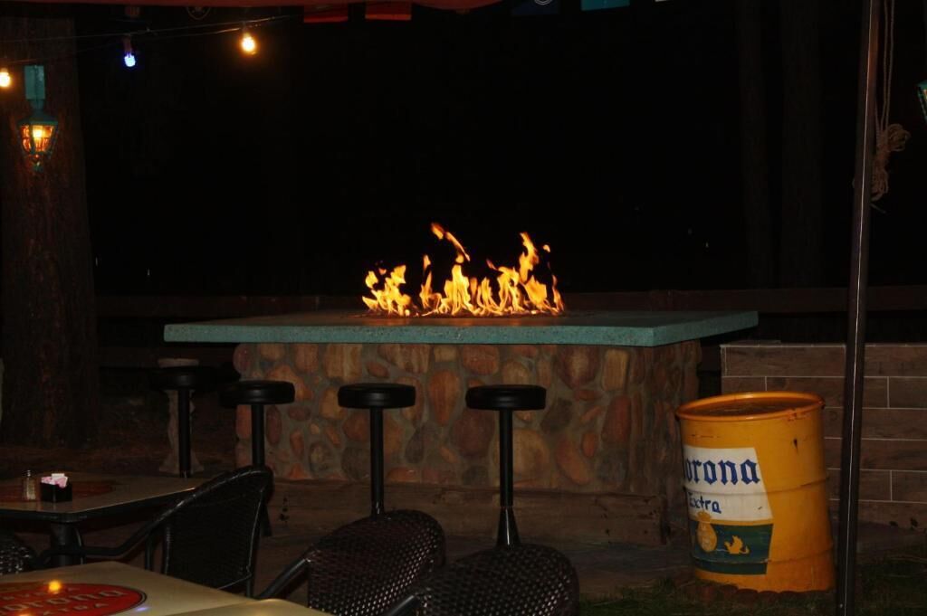 An outdoor bar area with a stone table and stools, a fire feature, and a Corona Extra barrel.