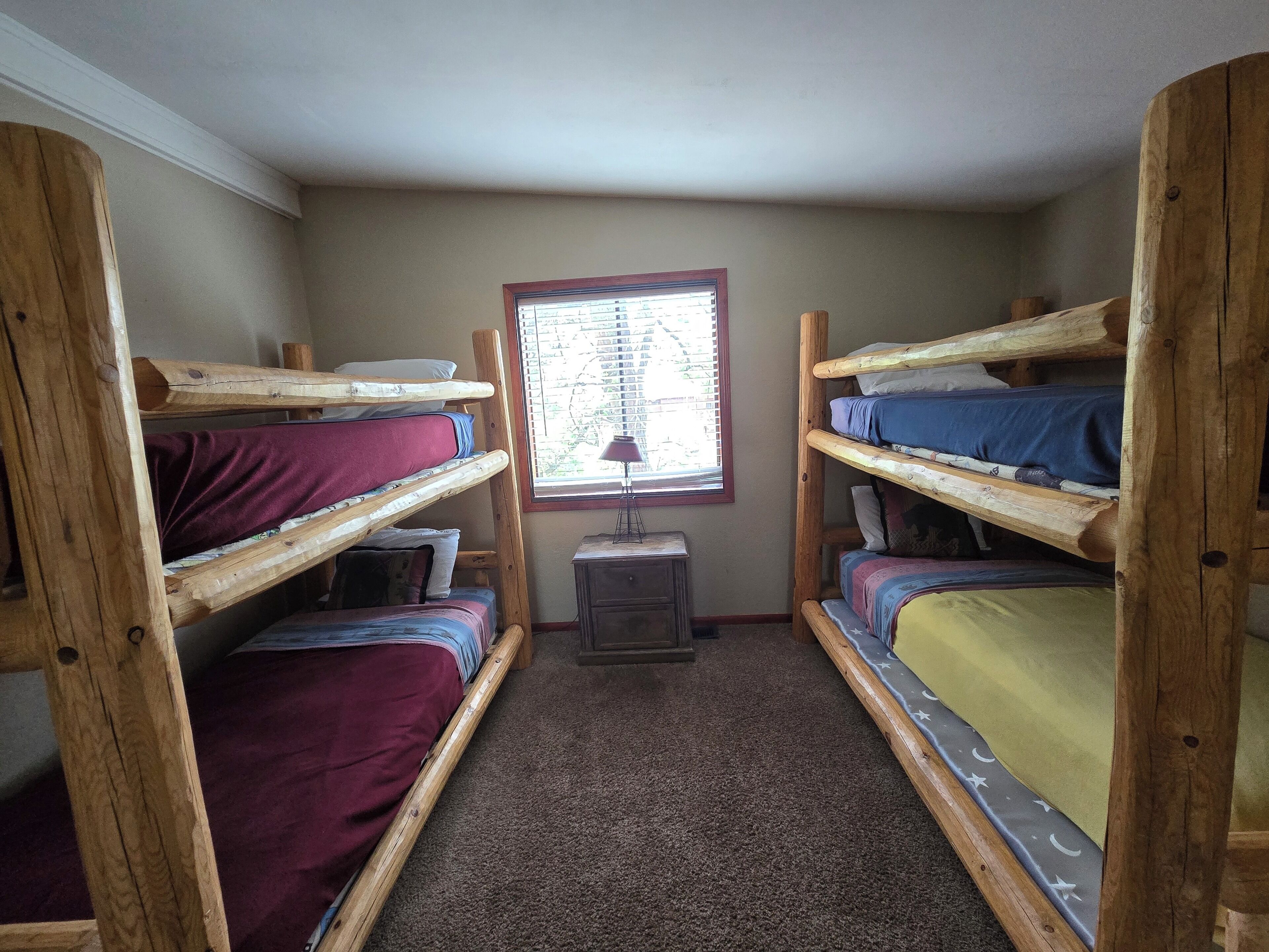 A dormitory room with bunk beds, a window with blinds, and a small desk with a lamp.