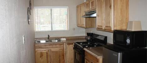 A kitchen with wooden cabinets, a stove, a microwave, and a sink.