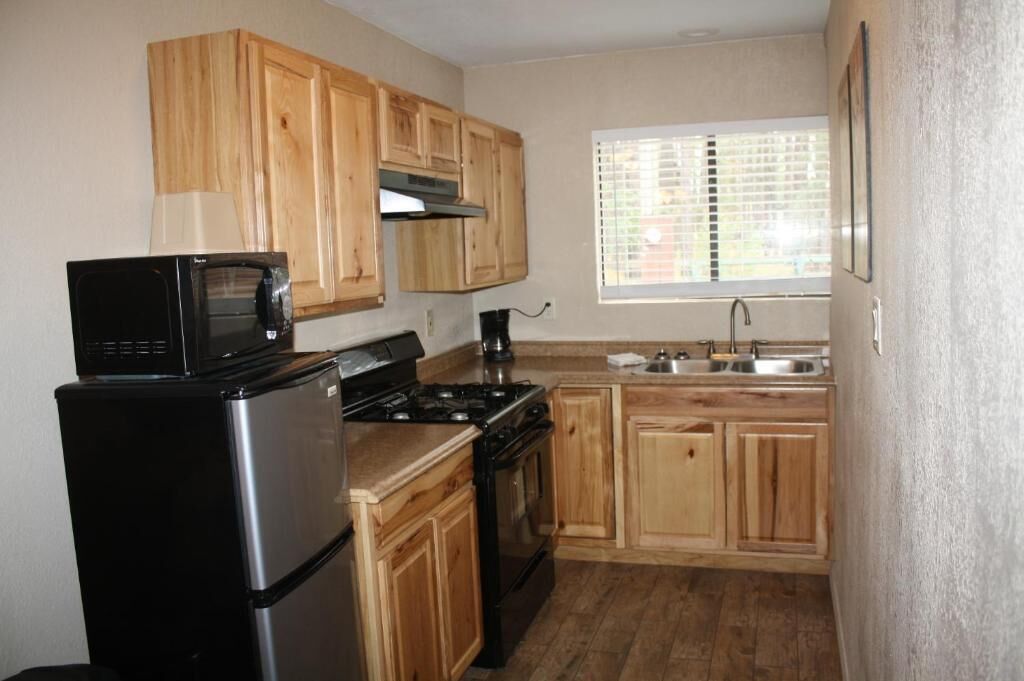 Une cuisine de taille réduite, dotée de meubles en bois, d’un réfrigérateur noir, d’une cuisinière et d’un four à micro-ondes.