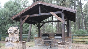A wooden gazebo with a metal roof, stone walls, and two barbecue grills. - Lumbermens Village (Lakeside)