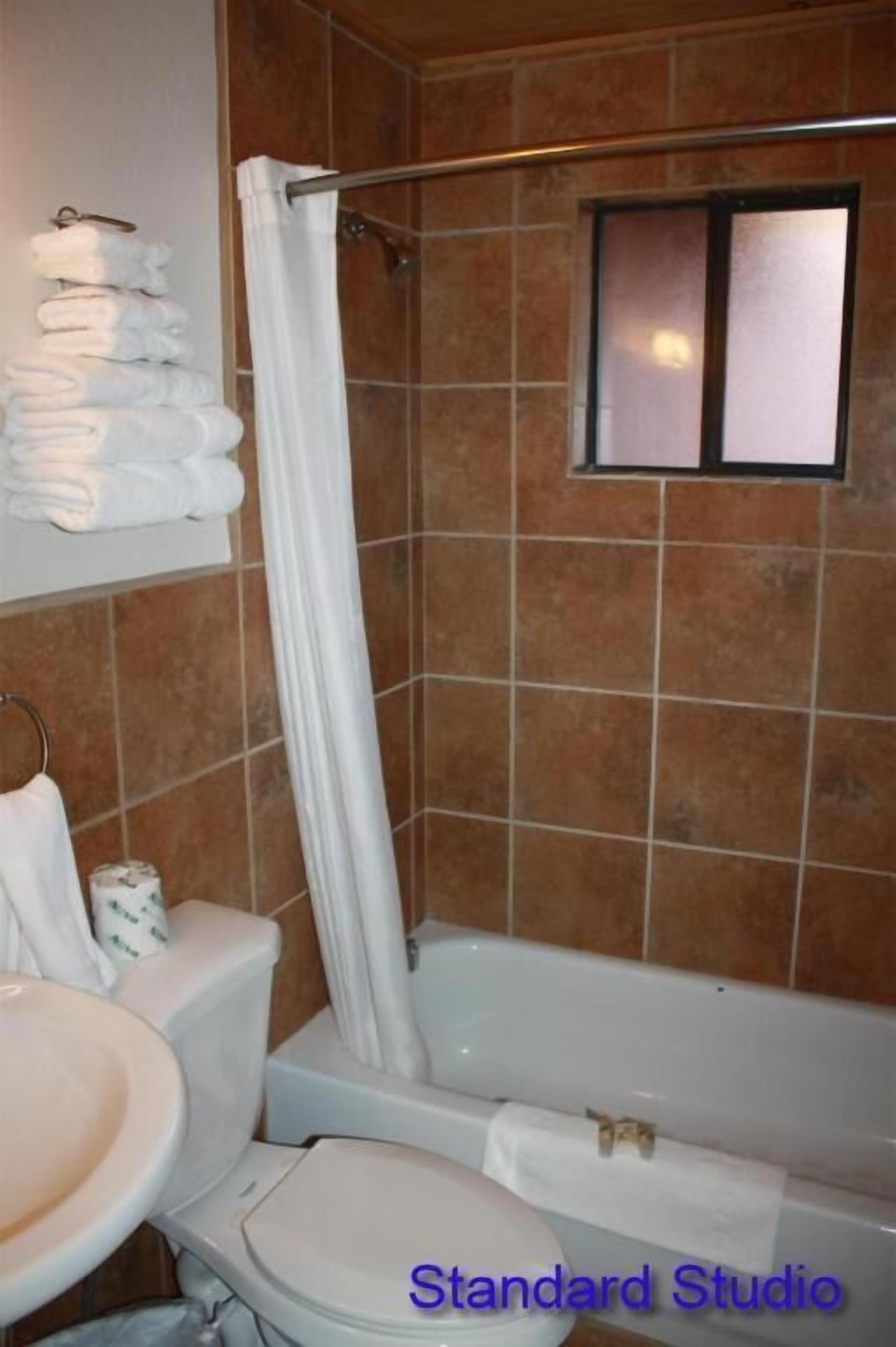 A bathroom with a toilet, sink, and bathtub. There is a towel rack with folded towels and a window above the bathtub.