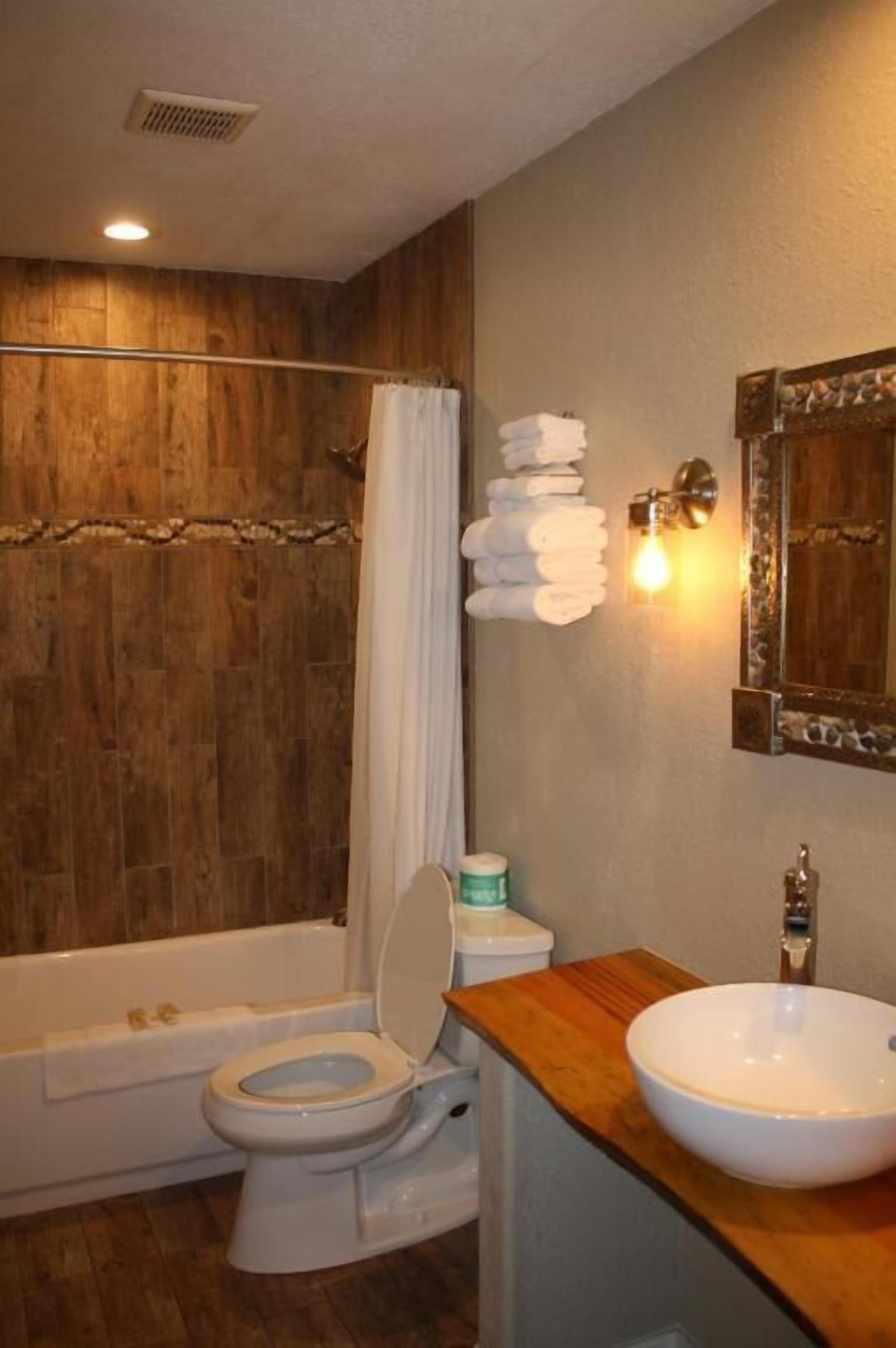 A bathroom with a wooden wall, a bathtub, a toilet, and a sink with a mirror above it.