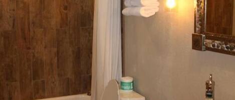 A bathroom with a wooden wall, a bathtub, a toilet, and a sink with a mirror above it.