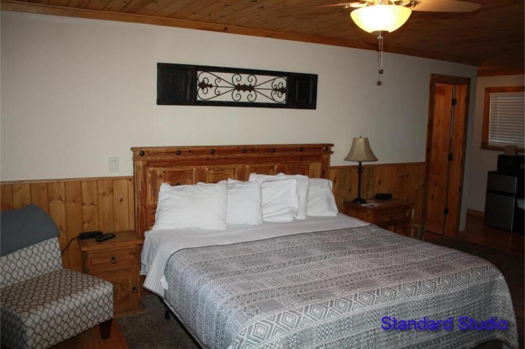 A bedroom with a wooden headboard, a patterned bedspread, a nightstand with a lamp, and a chair.