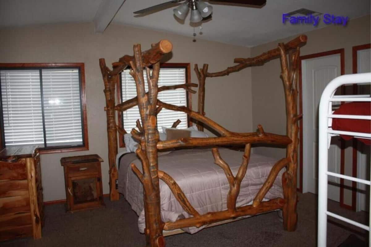 A rustic bedroom with a four-poster bed made of wood, a ceiling fan, and a window with blinds.