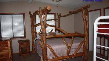 Um quarto rústico com cama de dossel de madeira, ventilador de teto e janela com persianas.