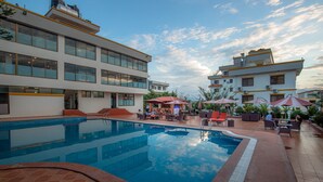 Ein Schwimmbecken mit gefliestem Sonnendeck, Sitzgelegenheiten im Freien und Blick auf die umliegenden Gebäude.