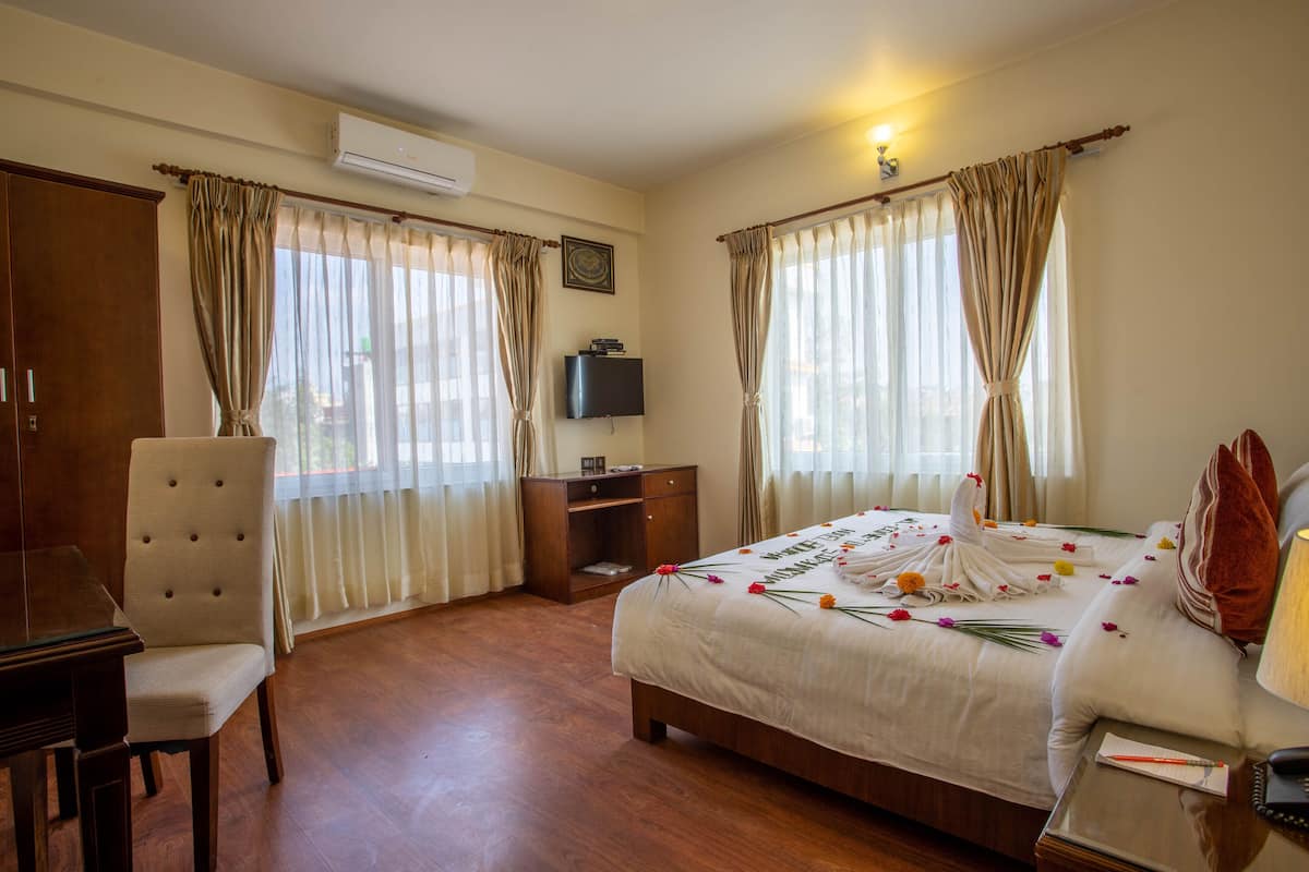 Quarto de hotel com cama, escrivaninha, cadeira e televisão.