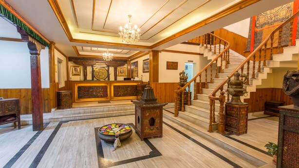 Eine prachtvolle Lobby mit Marmorboden, einem großen Kronleuchter, einer Treppe und einer dekorativen Blumenschale.