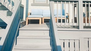 A wooden staircase leading to a covered deck with blue cushioned seating and a potted plant.