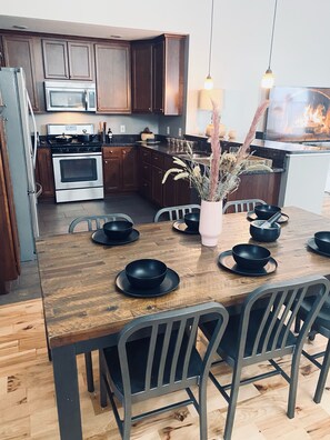 A modern kitchen with wooden cabinets, stainless steel appliances, and a dining table set with black bowls and plates.