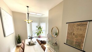 A dining area with a wooden table, chairs, a hanging light fixture, a potted plant, and a wall-mounted map.