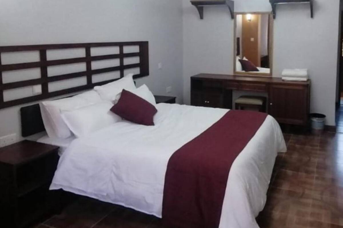 A hotel room with a bed, a nightstand, a dresser, and a mirror.
