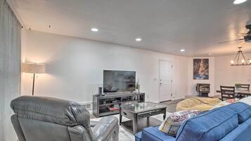 A modern living room with a leather sofa, a blue couch, a coffee table, a TV on a stand, and a dining area with a table and chairs.