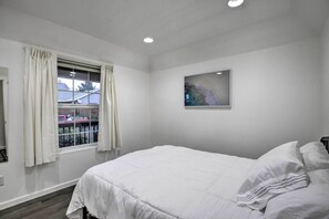 Quarto com uma cama grande, janela com cortinas, luminária no teto e um quadro na parede.
