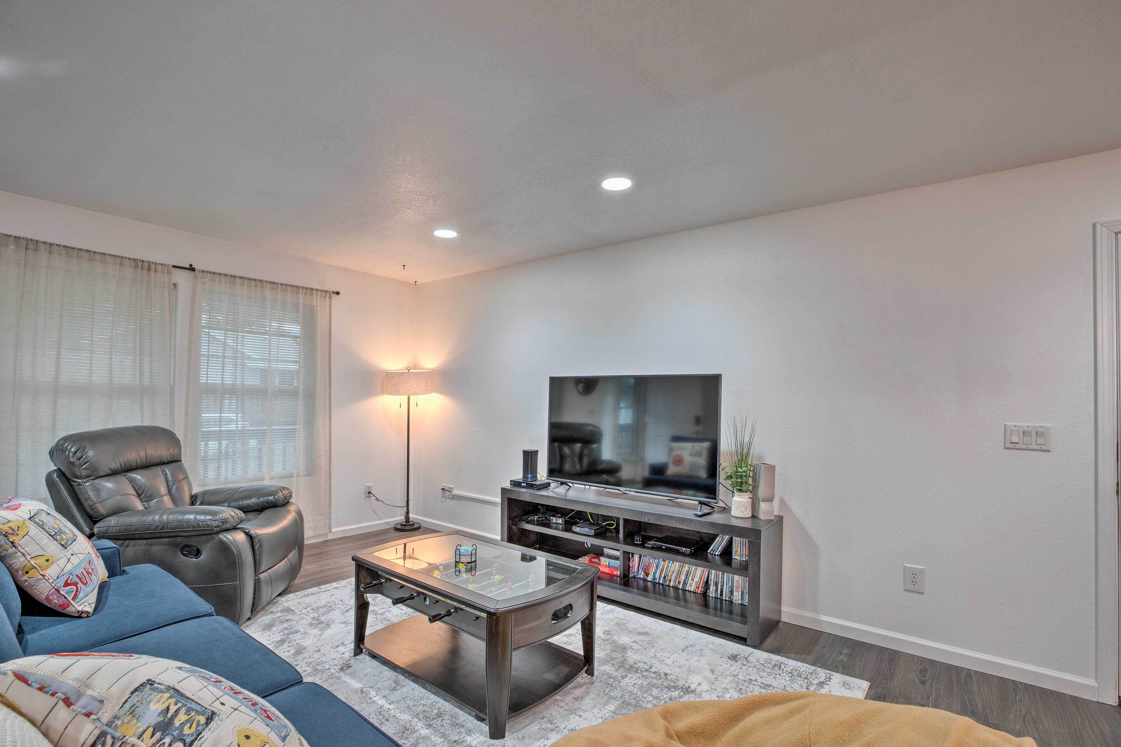 A modern living room with a leather recliner, a glass coffee table, a flat-screen TV, and a bookshelf.