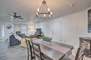 Uma sala de estar moderna com uma mesa de jantar, cadeiras, um sofá, um ventilador de teto, um lustre e uma lareira.