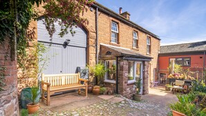 A stone building with a wooden bench, potted plants, and a cobblestone pathway.