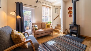 A cozy living room with a sofa, a chair, a fireplace, and a window with blinds.