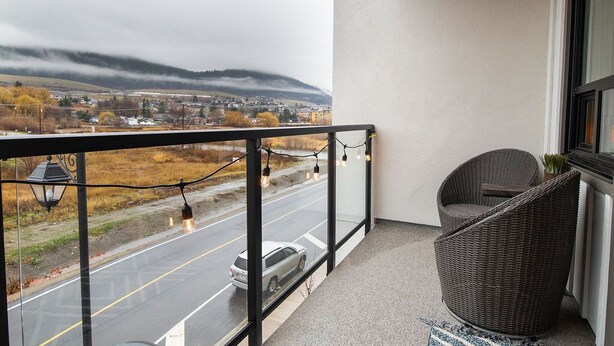 A balcony with a wicker chair, a view of a road, and a distant mountain range. - Lake Okanagan beach condo w/ private buoy, AC, heated outdoor pool, patio, SUPs (Vernon)