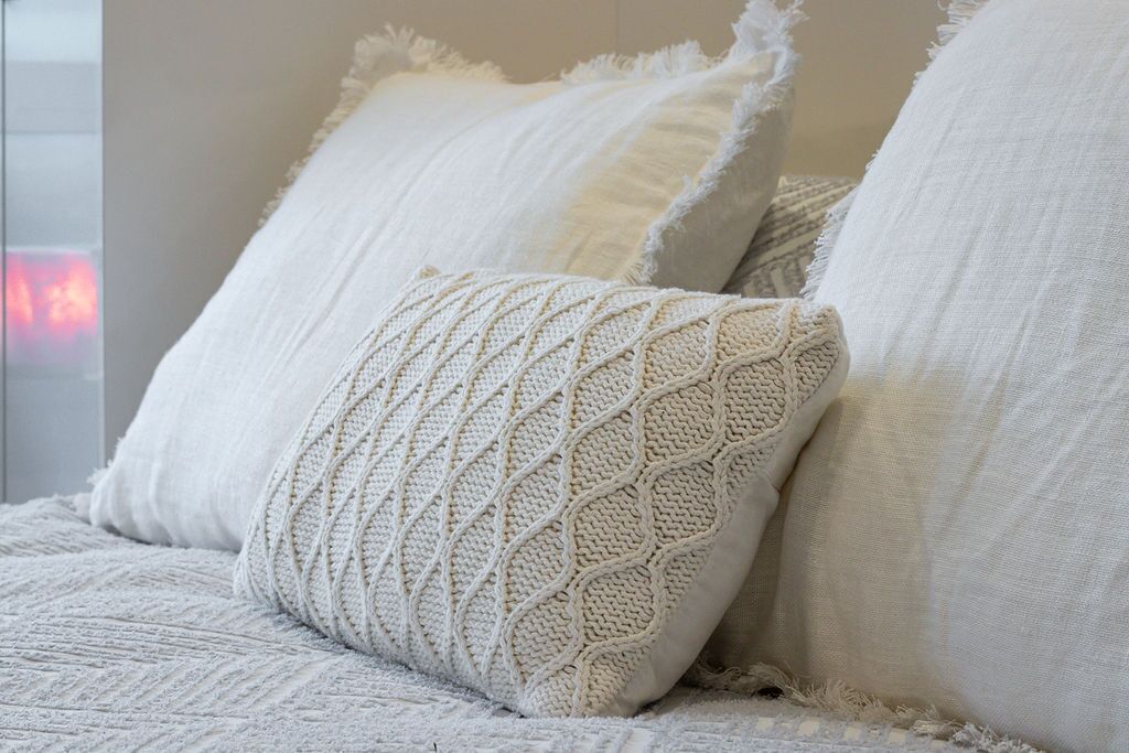 Een bed met witte beddengoed en een gebreide sierkussen.