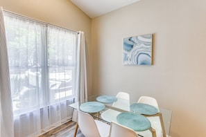 Un comedor con una mesa de vidrio, sillas blancas y individuales azules.