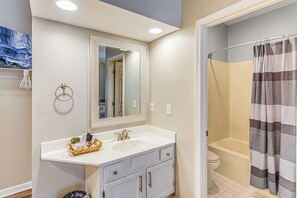 Un baño con tocador blanco, un espejo grande, una bañera y una cortina de ducha.