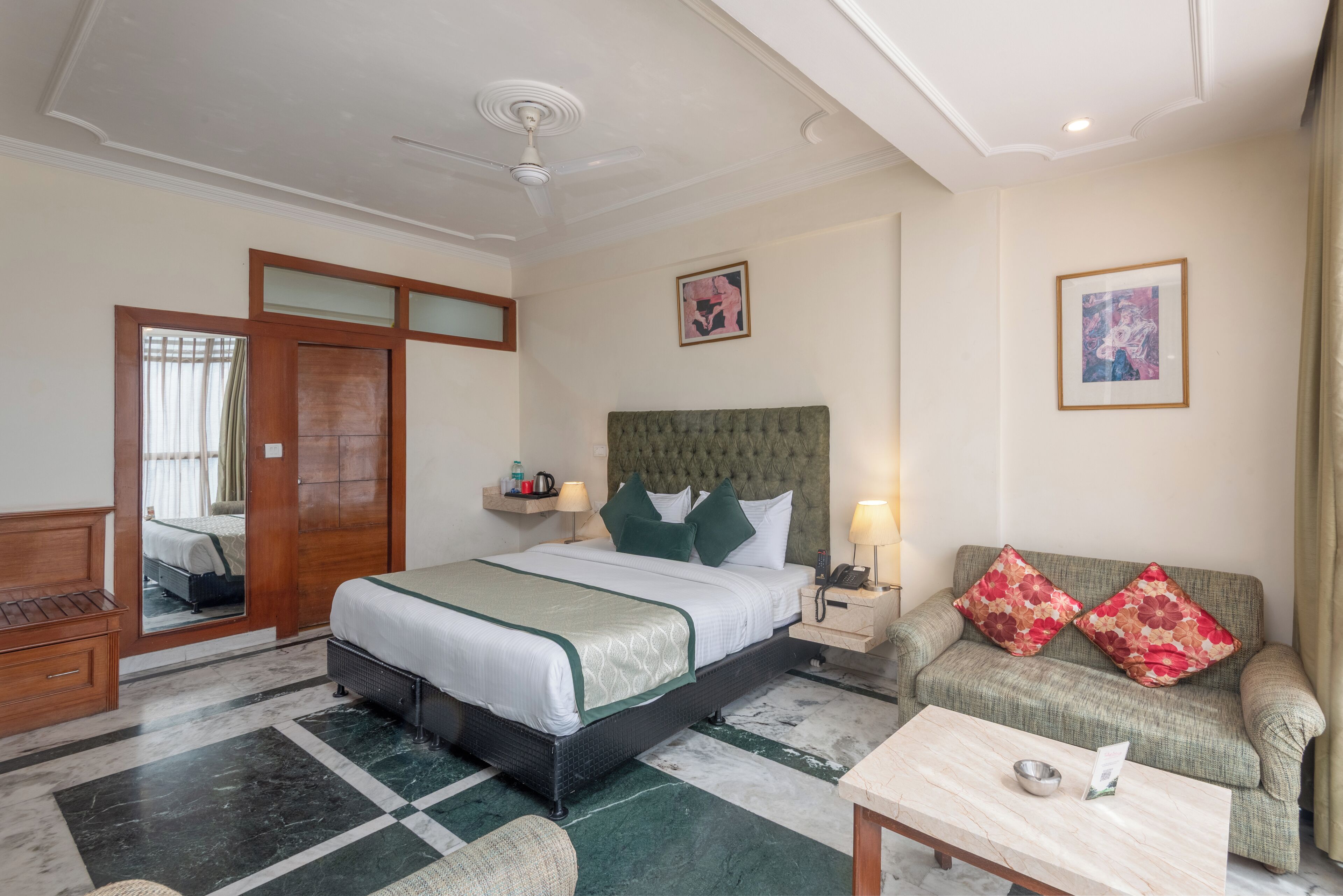 Una habitación de hotel con cama, sofá, mesa de centro, mesita de noche y espejo.
