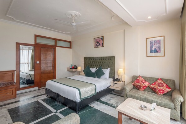 A hotel room with a bed, a sofa, a coffee table, a nightstand, and a mirror.