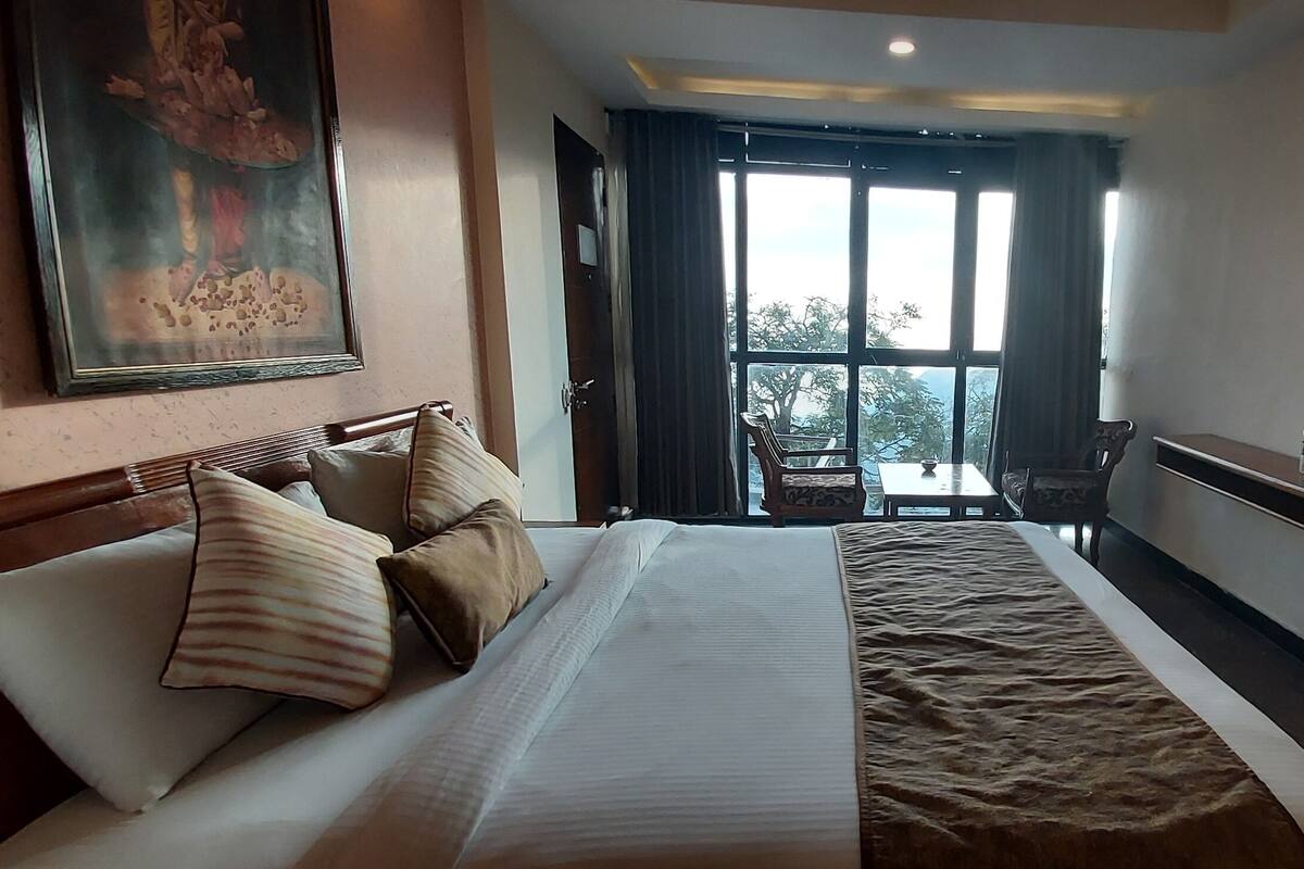 Ein Hotelzimmer mit einem großen Bett, einem Fernseher, einem Schreibtisch und einem Fenster mit Vorhängen.