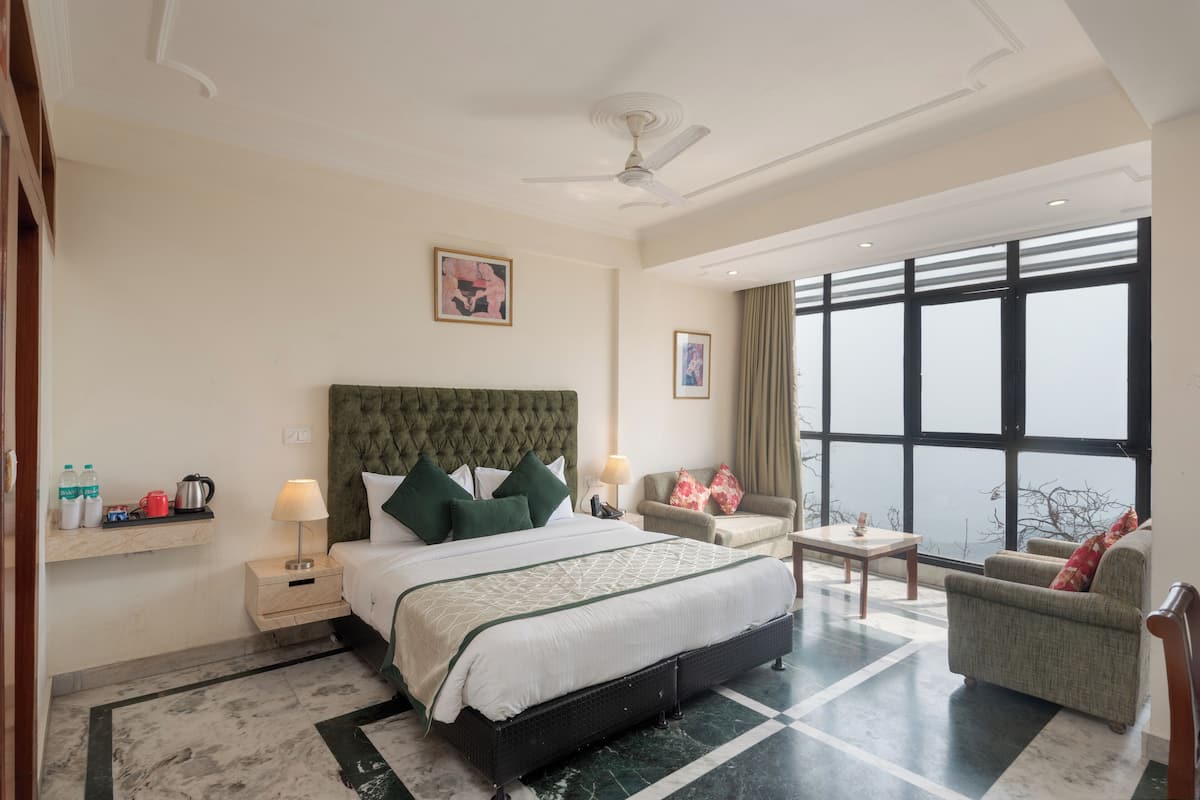 Ein Hotelzimmer mit einem großen Bett, einer Sitzecke mit Sofa und Sessel, einem kleinen Tisch und einem großen Fenster mit Blick.