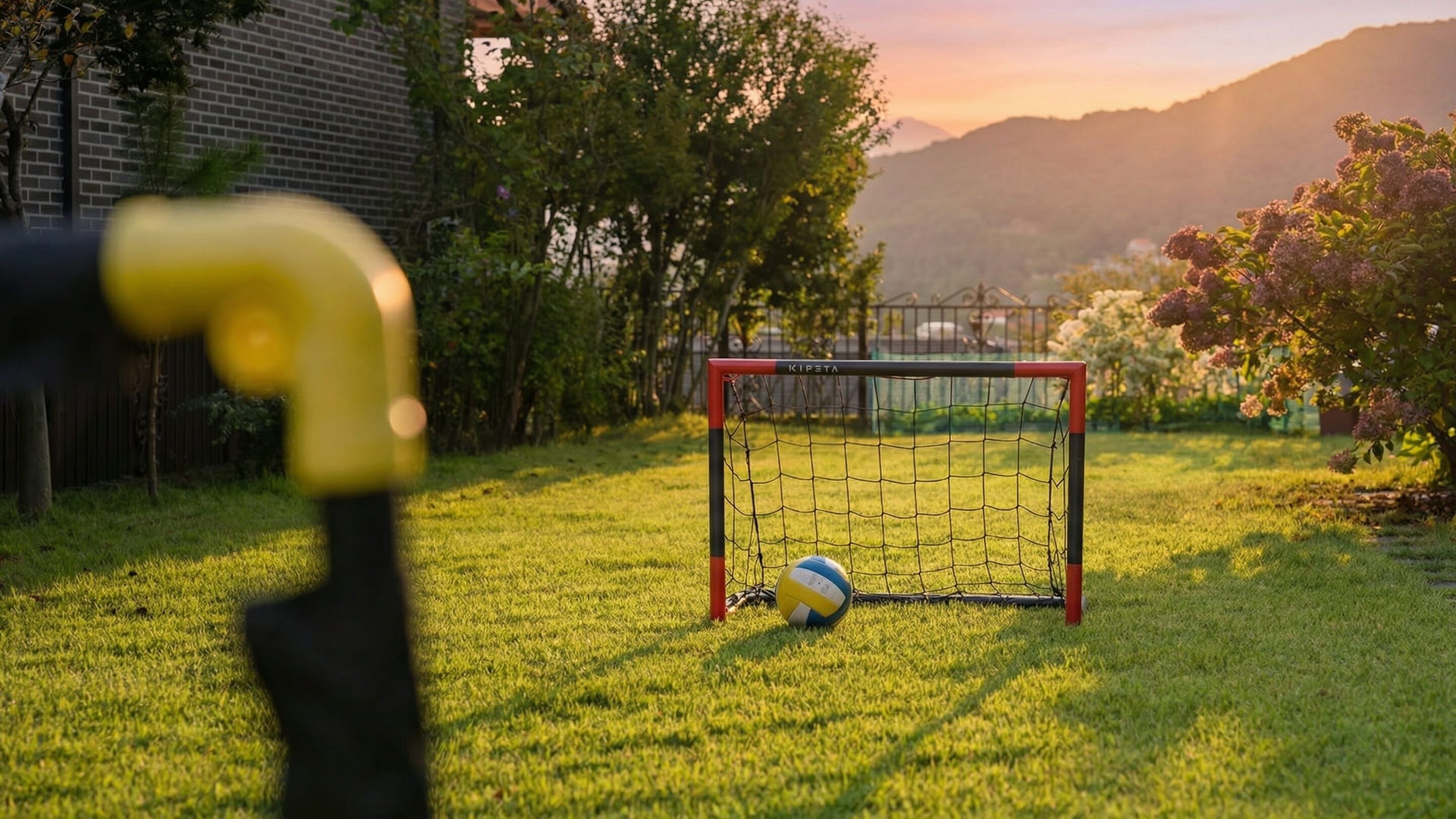 Un but de football, situé dans une zone herbeuse, avec un filet, un ballon et un objet jaune au premier plan.