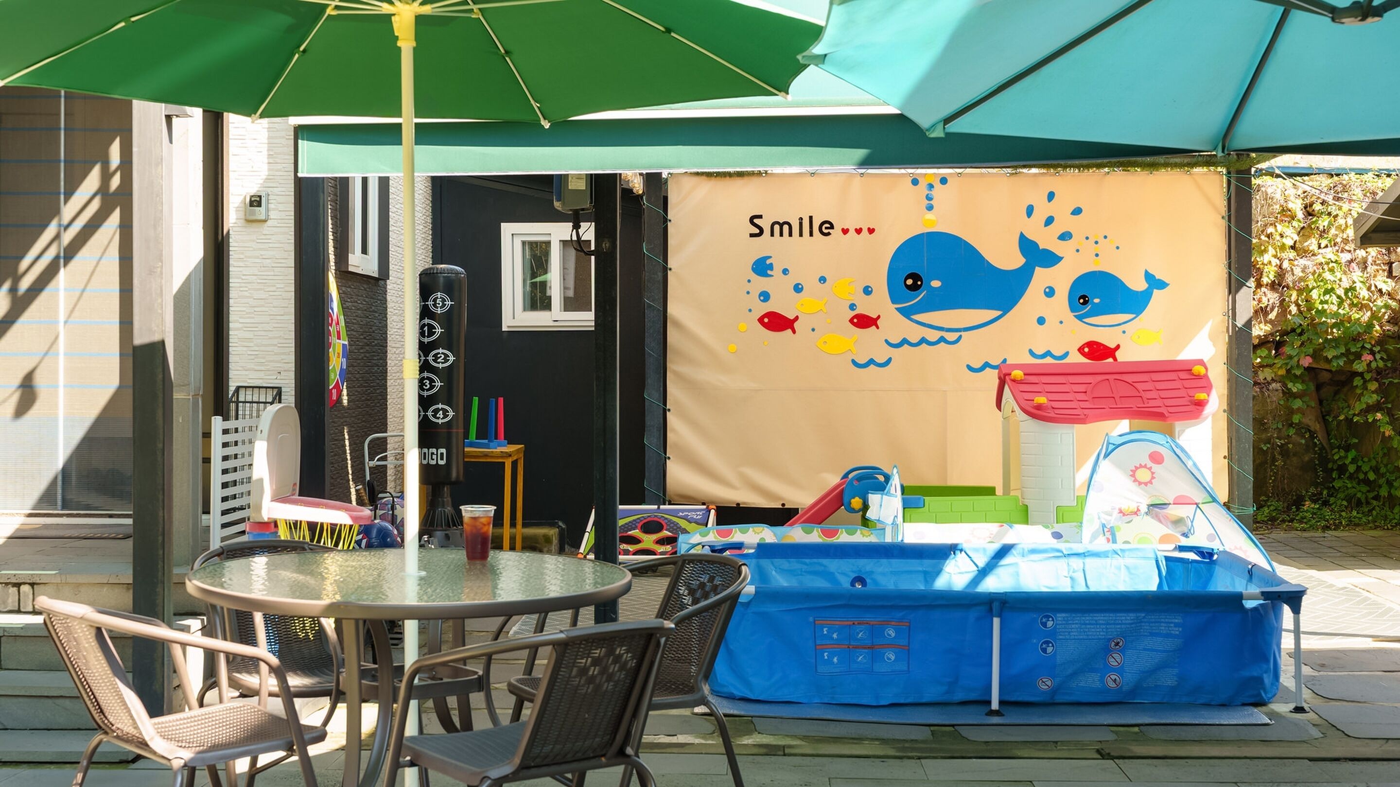An outdoor seating area with a table and chairs, a blue play tent, and a banner with a whale and fish design.